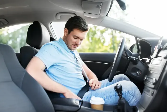 Driver in the front seat of a passenger car drawing the seat belt across the body.