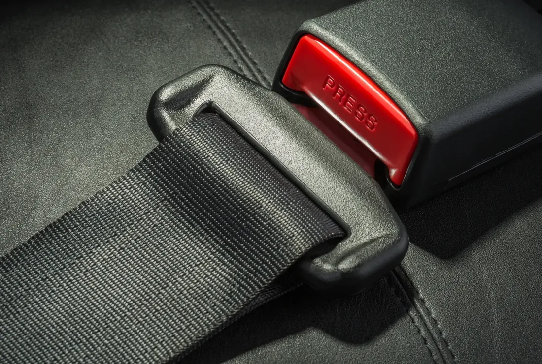 Detail of a seat belt assembly showing the woven webbing, the latch plate, the buckle receiver and its red release button.