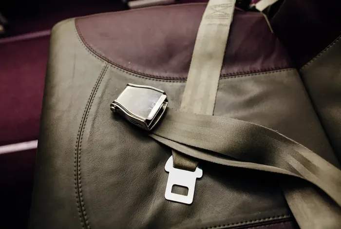 Lap belt with a metal lift-latch buckle laid across an olive-toned vehicle seat.